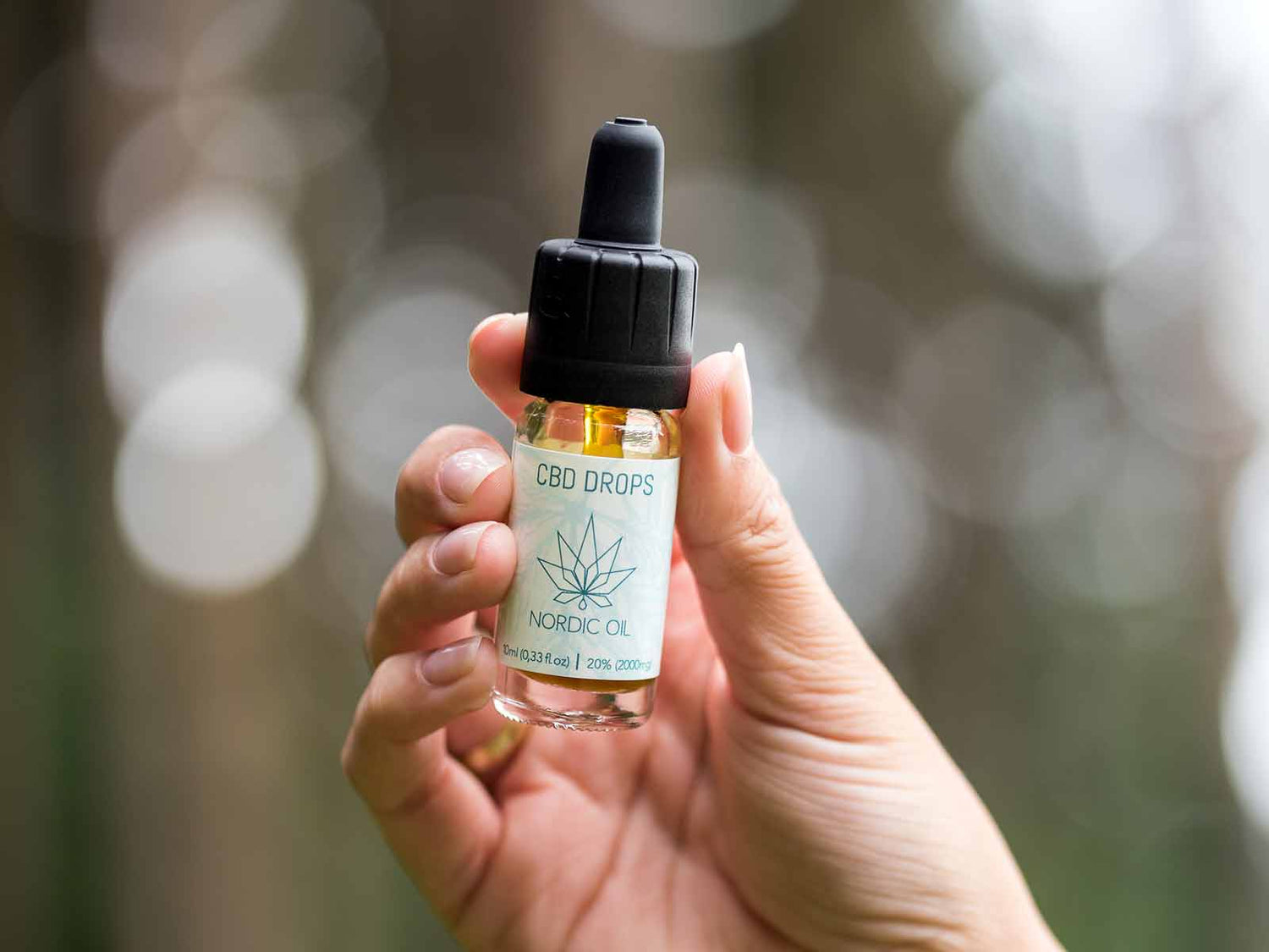 En kvinnas hand håller en flaska CBD Aroma Oil (15 %).